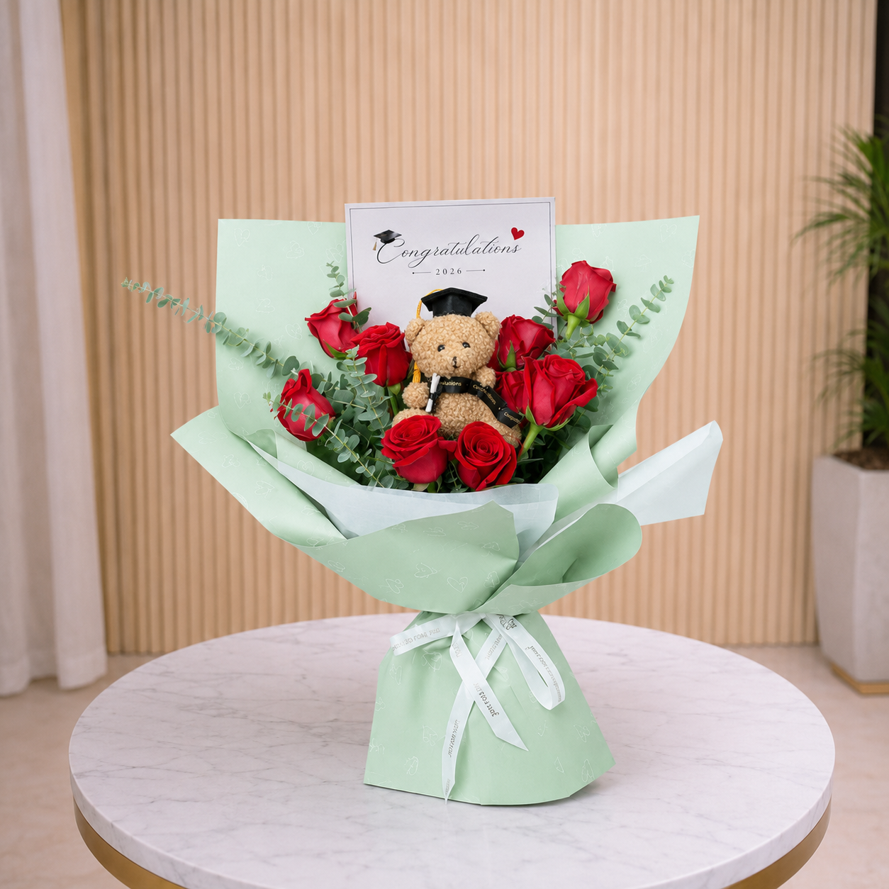 Bouquet of red roses with a teddy bear and 'Congratulations' card on a white table.