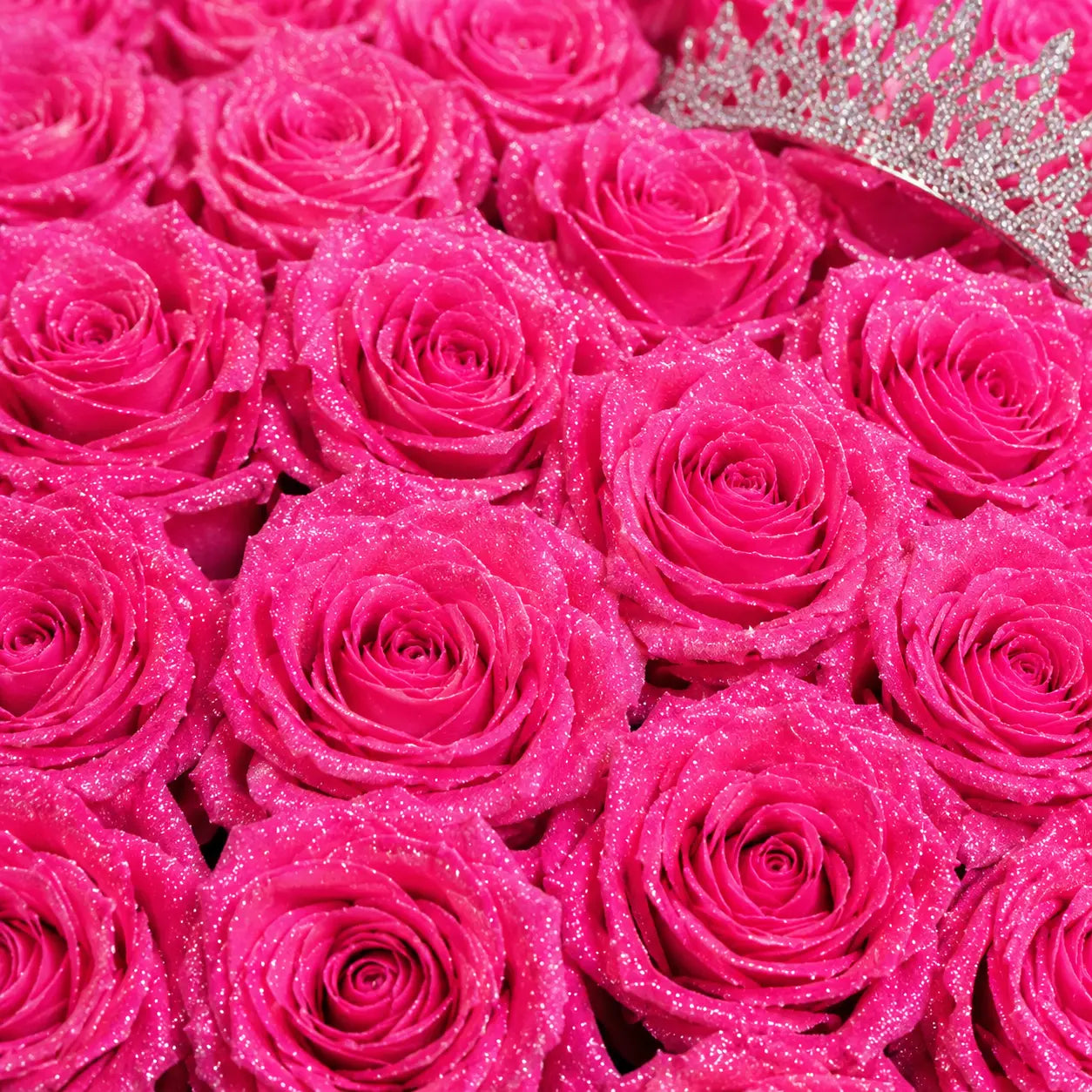 A close-up of a bouquet of bright pink glittery roses, with a silver tiara partially visible in the top right corner.