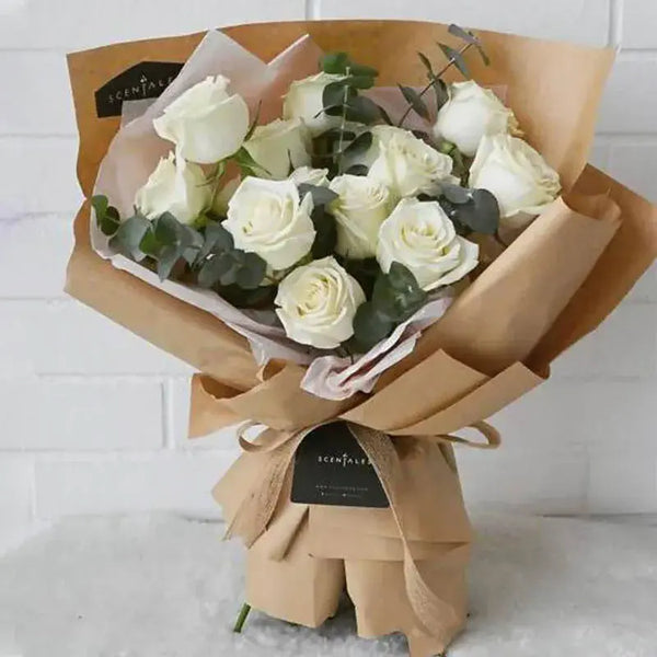 Bouquet of white roses wrapped in brown paper with a visible brand label on a light background.